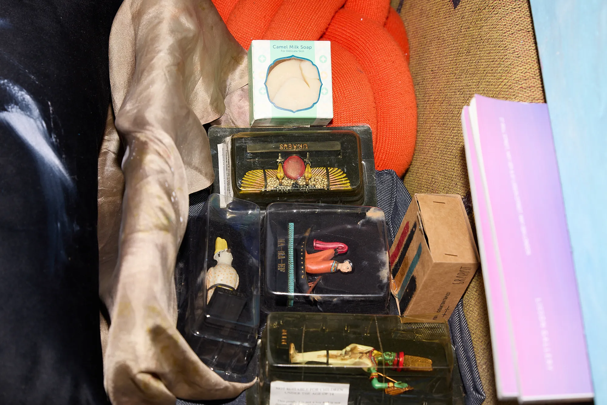 A dim close-up of small boxed keepsakes and soap tucked into folded fabric in Omar Kholeif's studio