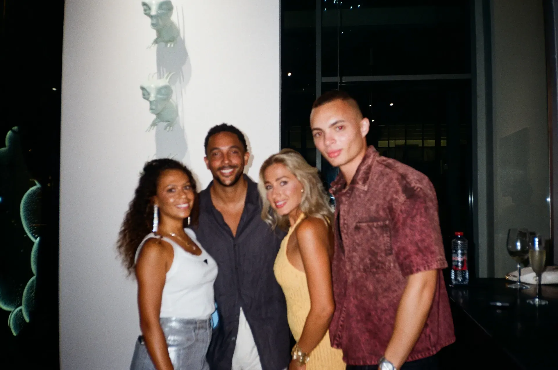 Four guests posing together in front of small alien-like sculptural figures mounted on the wall