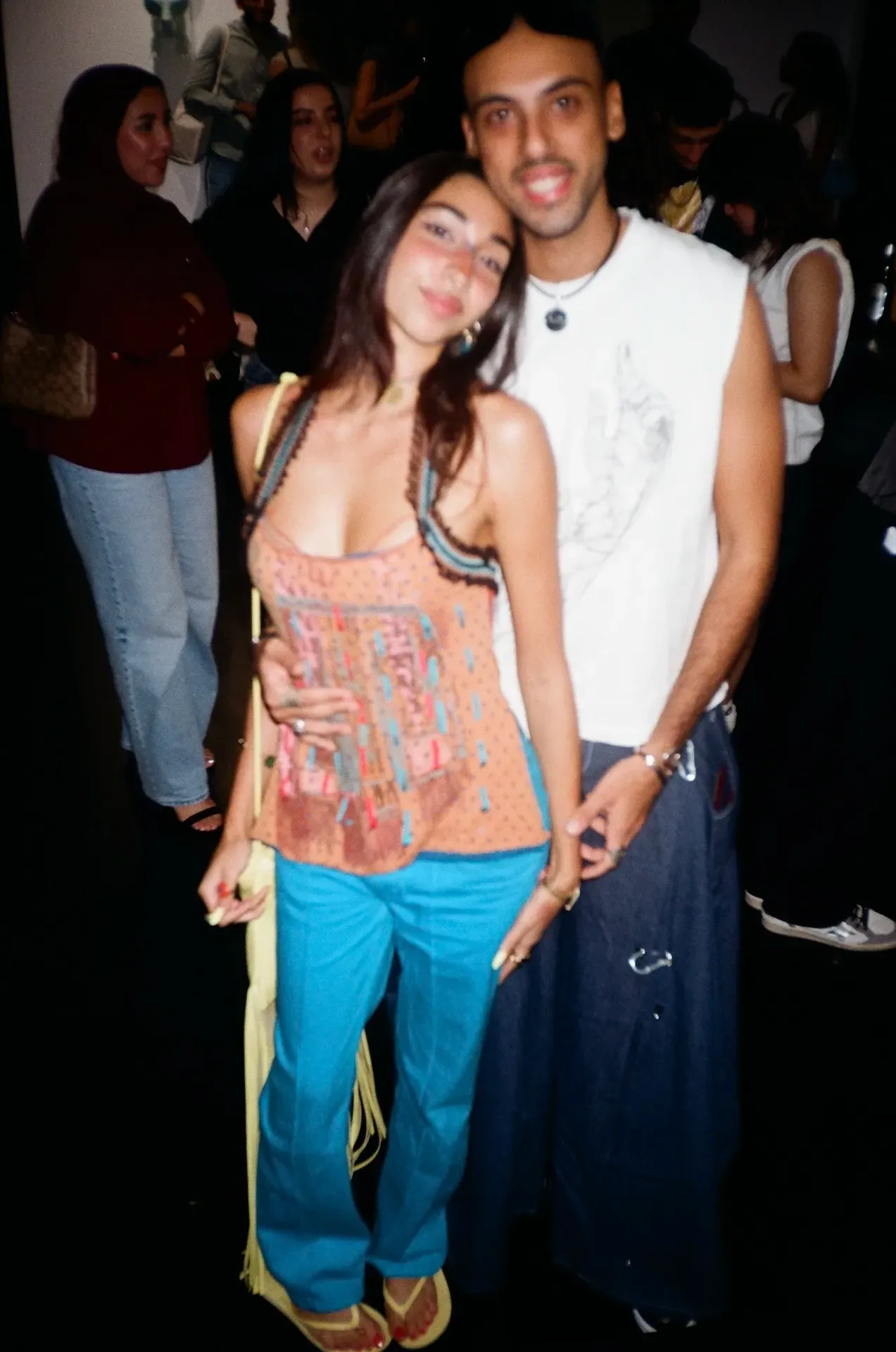 Two guests posing together at the opening, one in a printed halter top and blue trousers