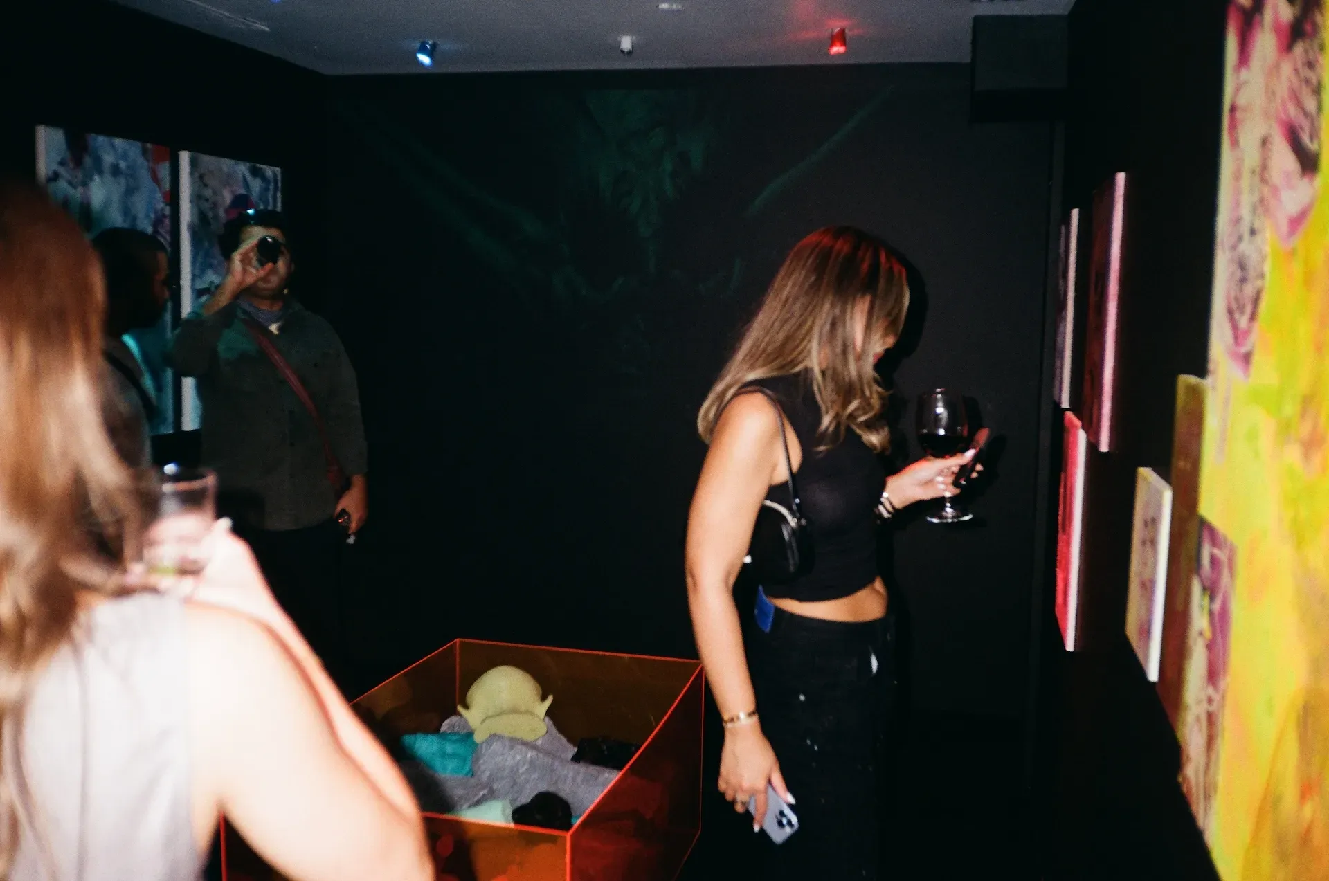 A guest photographing a display case of small sculptures in a dark gallery corner hung with paintings
