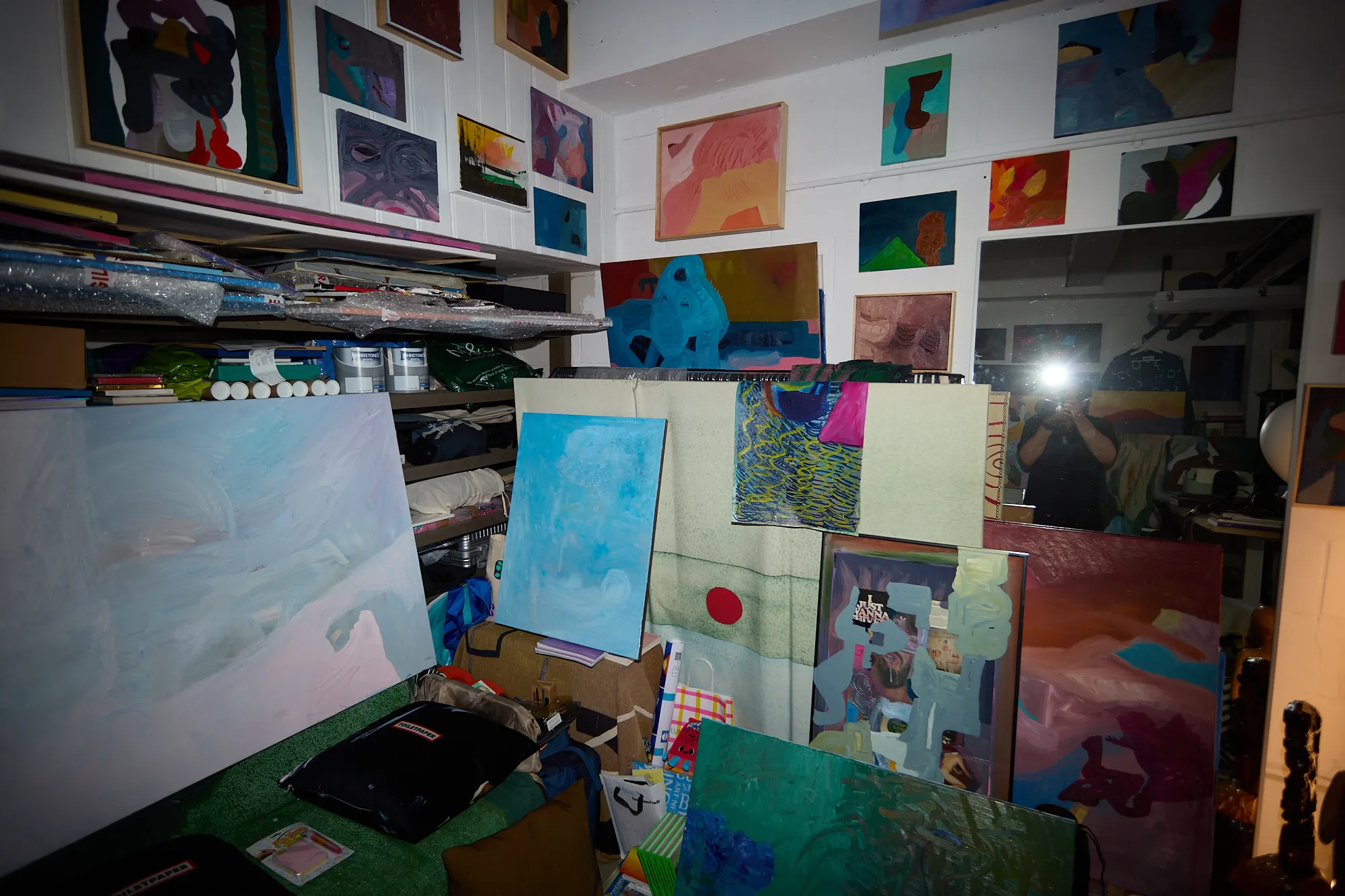 A dense corner of Omar Kholeif's studio, paintings stacked and hung from every surface beneath a small watching portrait, before it was cleared